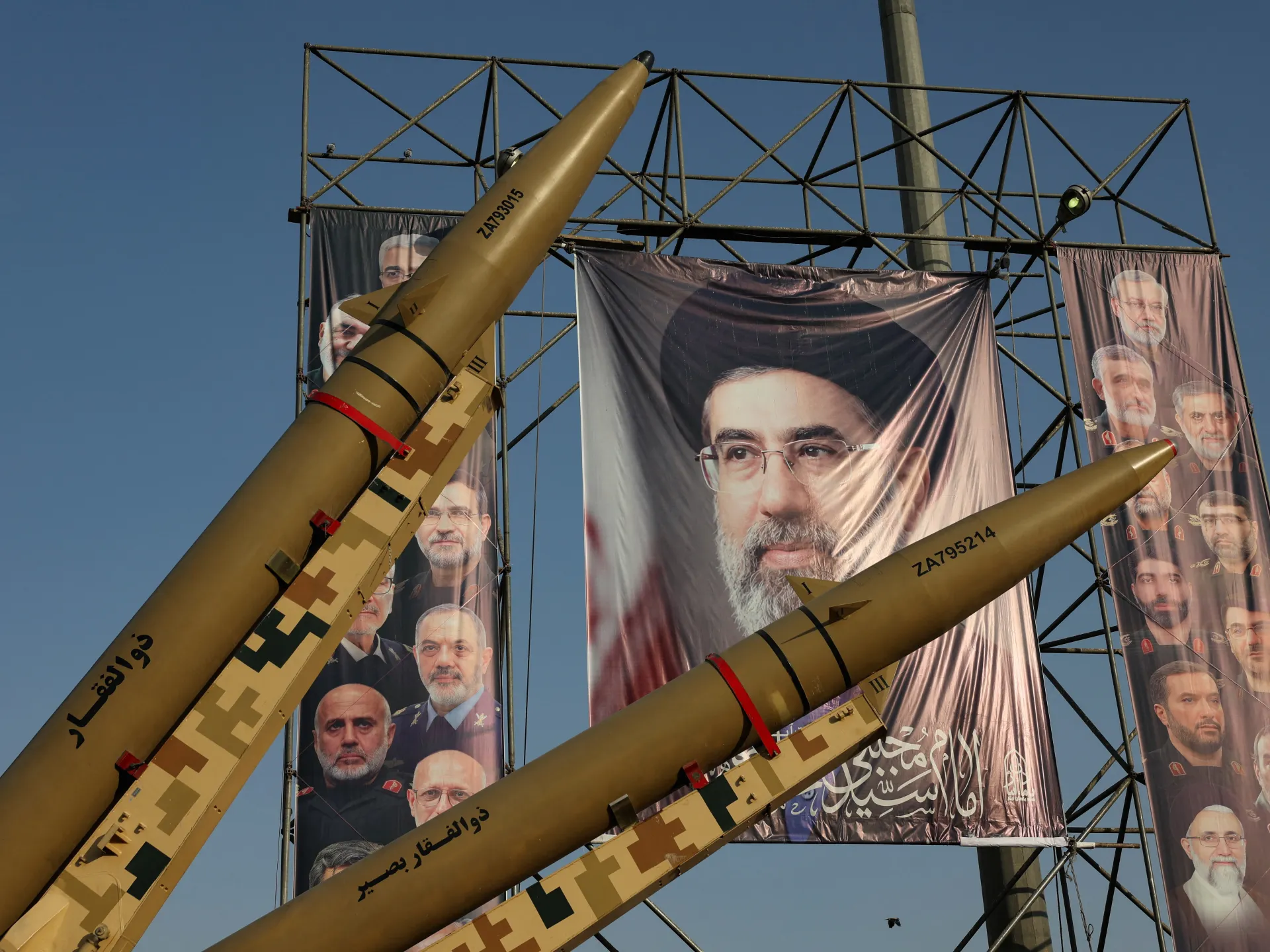 Two missiles displayed before large portrait banners, with a metal framework and blue sky behind them.