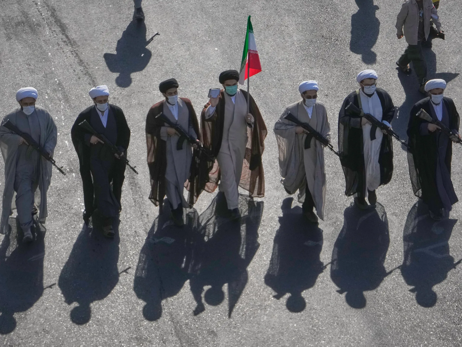 Masked men in clerical robes carry rifles while one holds an Iranian flag.