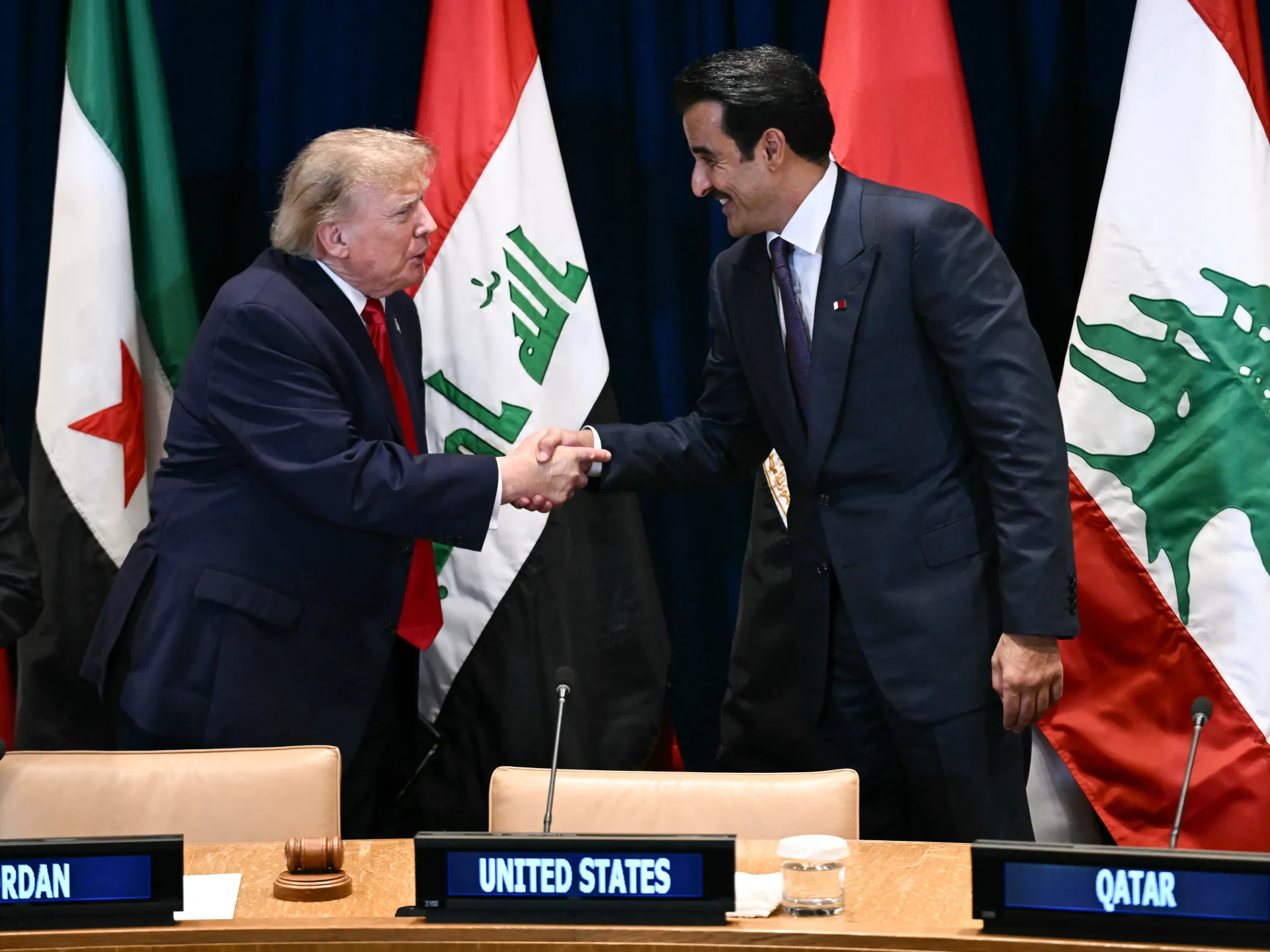 Two suited men shake hands in front of Iranian and United States flags at a conference table.