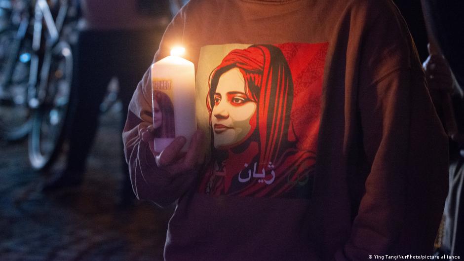 Person holding a lit candle while wearing a sweatshirt depicting a woman in a headscarf.