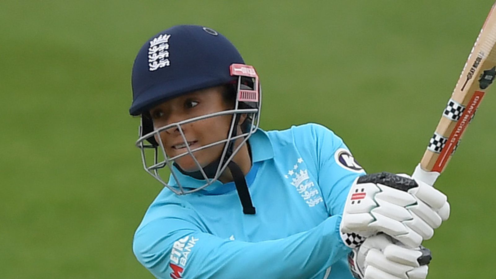 Cricketer in blue helmet and jersey swings a bat while wearing white gloves