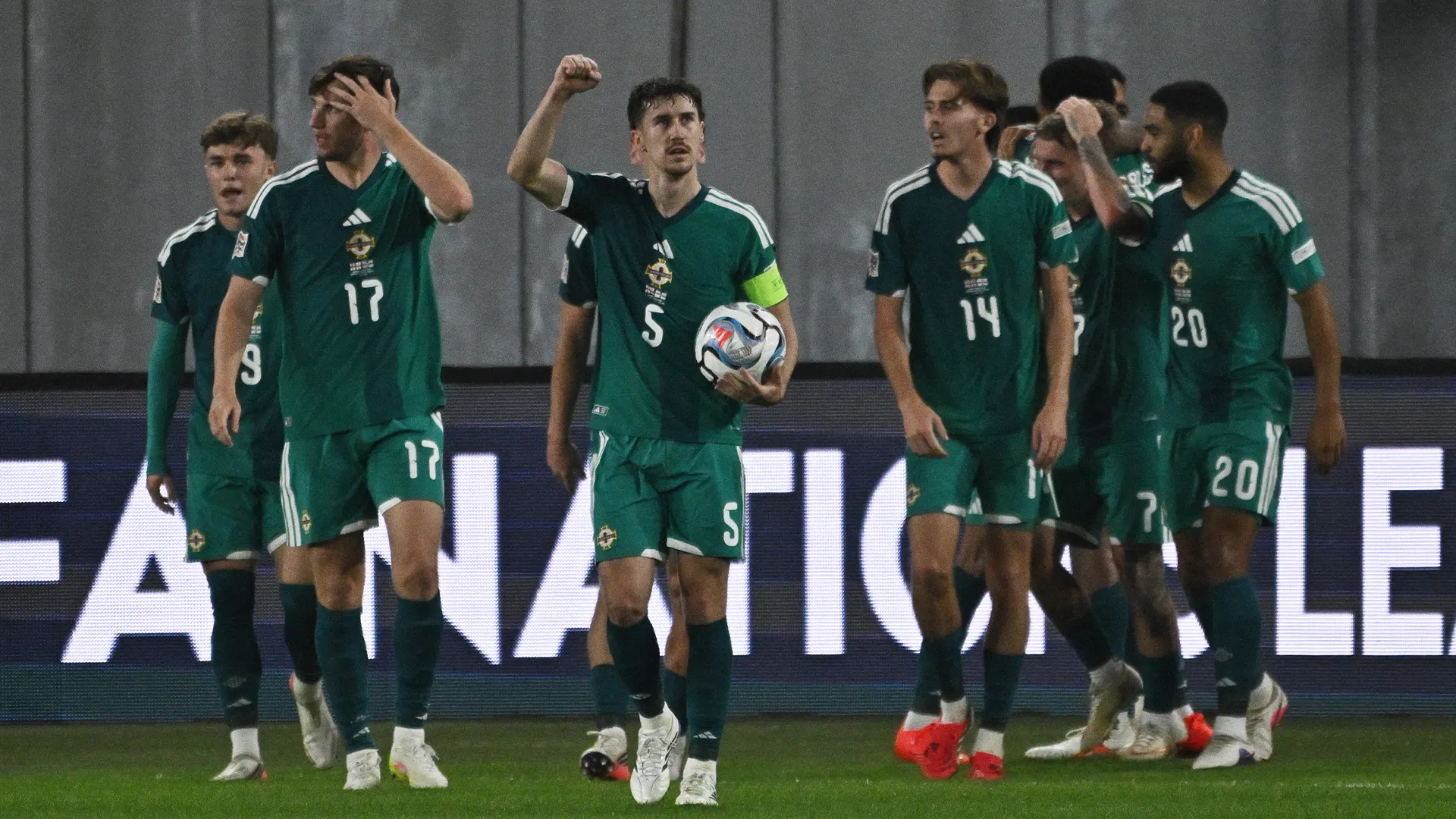 Northern Ireland players in green kits gather after a match, one holding a football.
