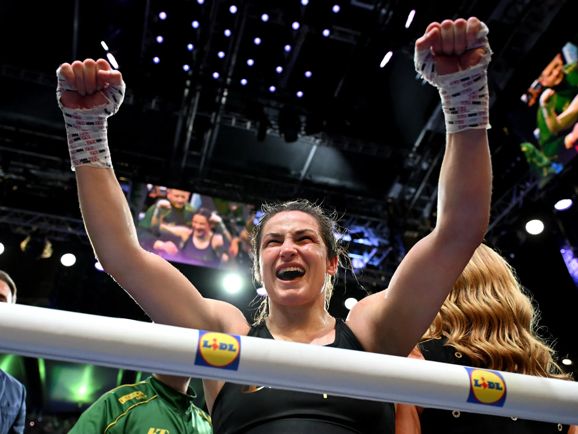 Boxer raises both wrapped fists in celebration inside a ring beneath bright arena lights