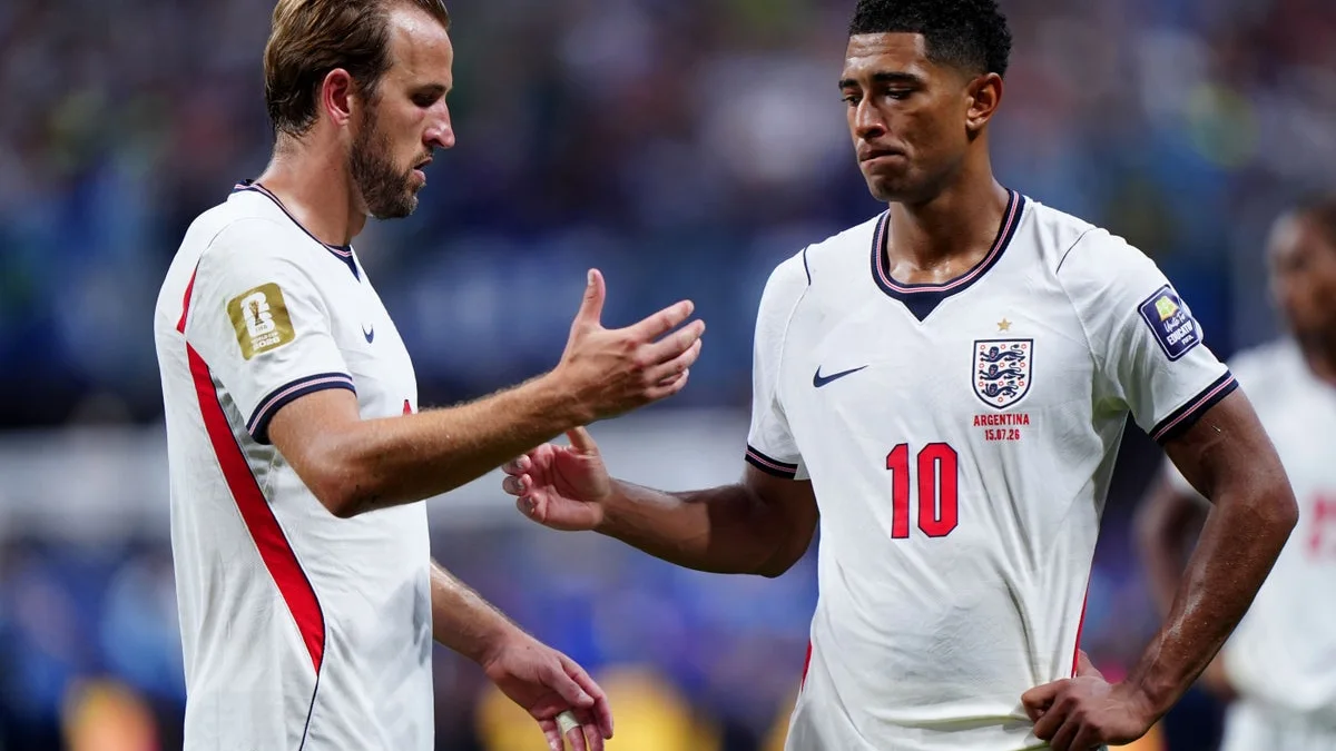 Two footballers in white England shirts gesture toward each other on the pitch.