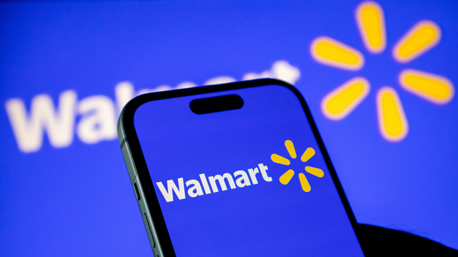 Smartphone displaying the Walmart logo against a blue background with a blurred Walmart sign.