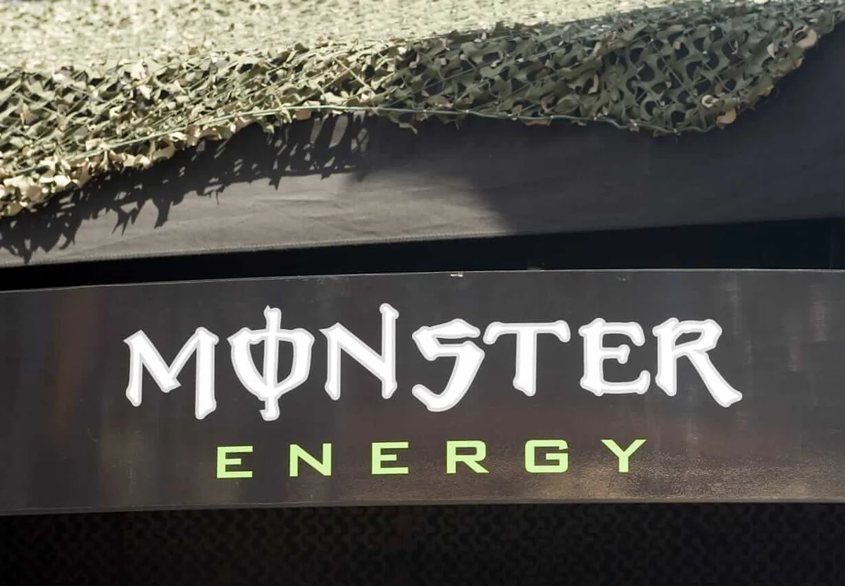 Monster Energy logo displayed on a dark panel beneath camouflage netting.