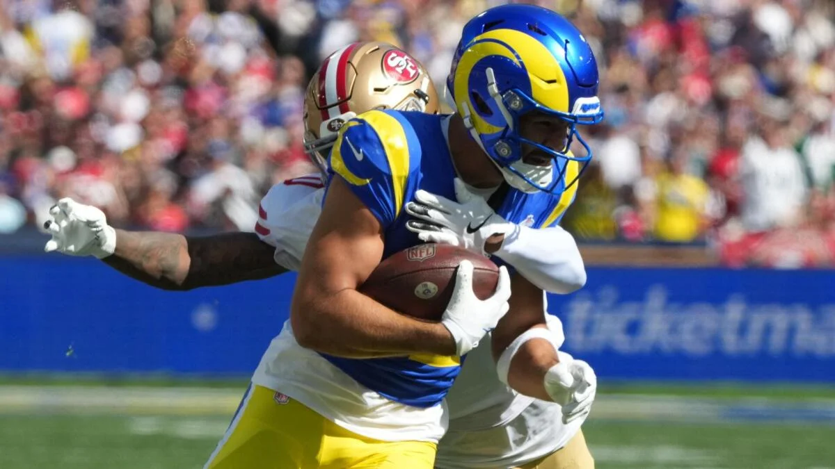 Rams receiver carrying football as a 49ers defender reaches around him during a game