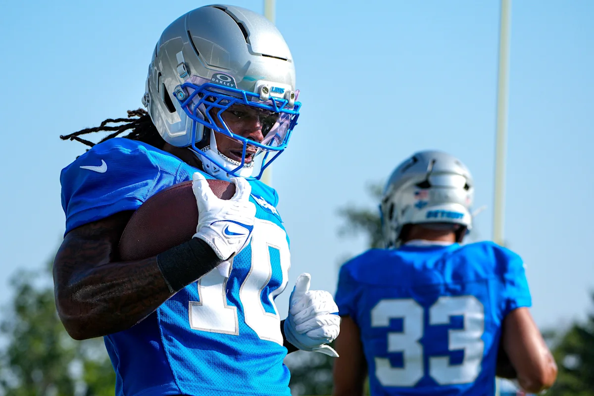 Football player in blue jersey and helmet runs with ball during outdoor practice.