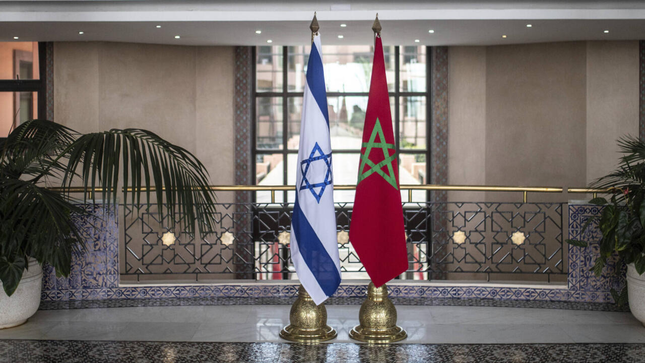 Israeli and Moroccan flags displayed side by side inside an ornate interior with plants and tiled decorations.