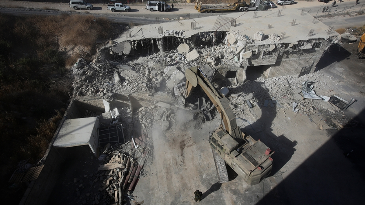 Excavator demolishes a concrete building amid rubble, viewed from above in a construction area.