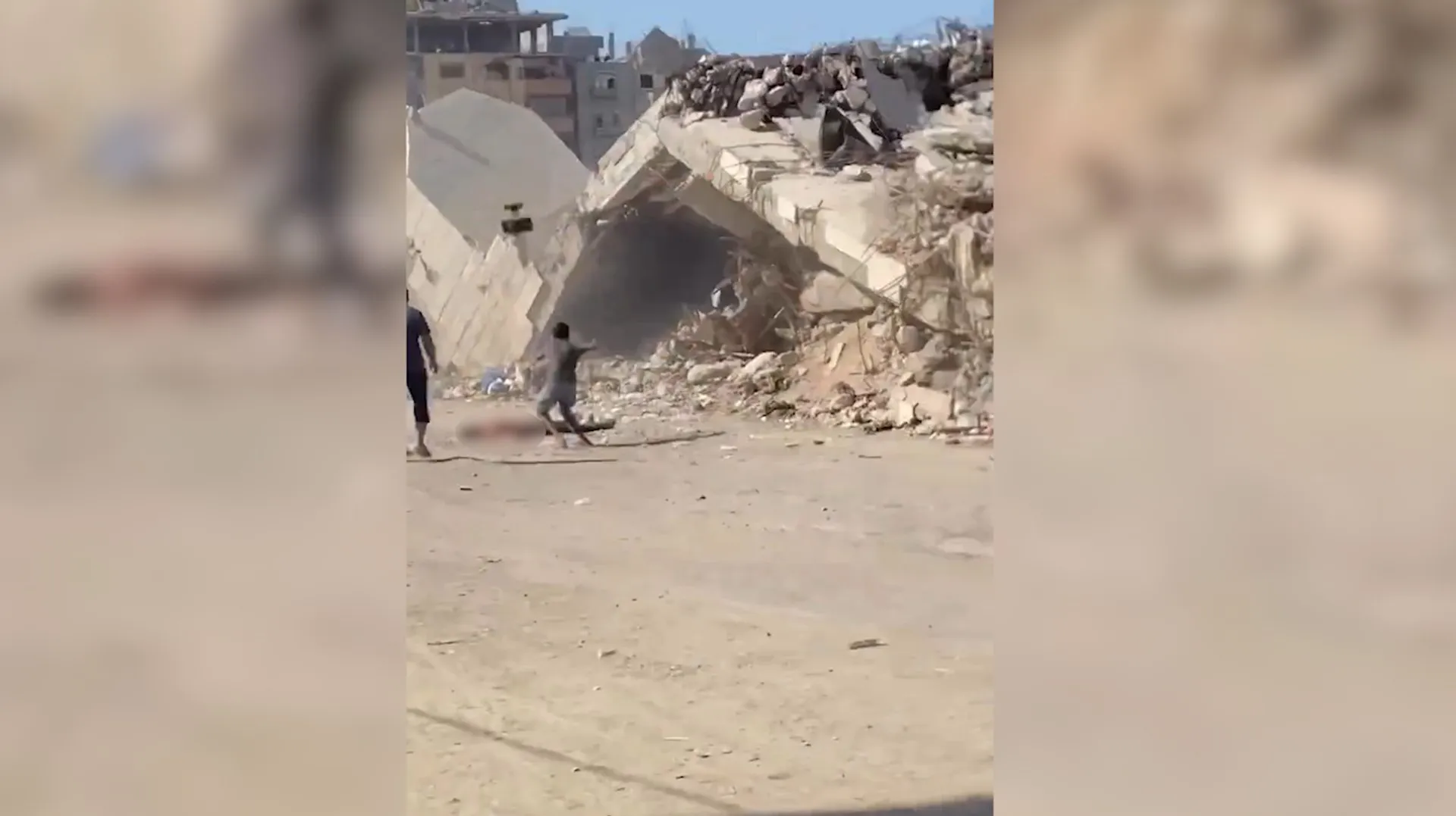 People walk beside the rubble of a collapsed concrete building in a dusty urban area.
