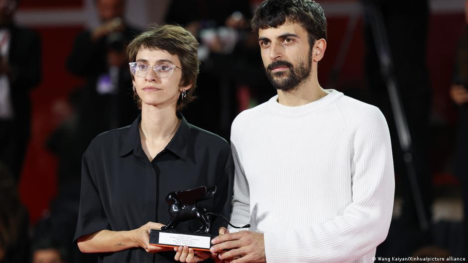 Two filmmakers pose together holding a black statuette and award plaque.