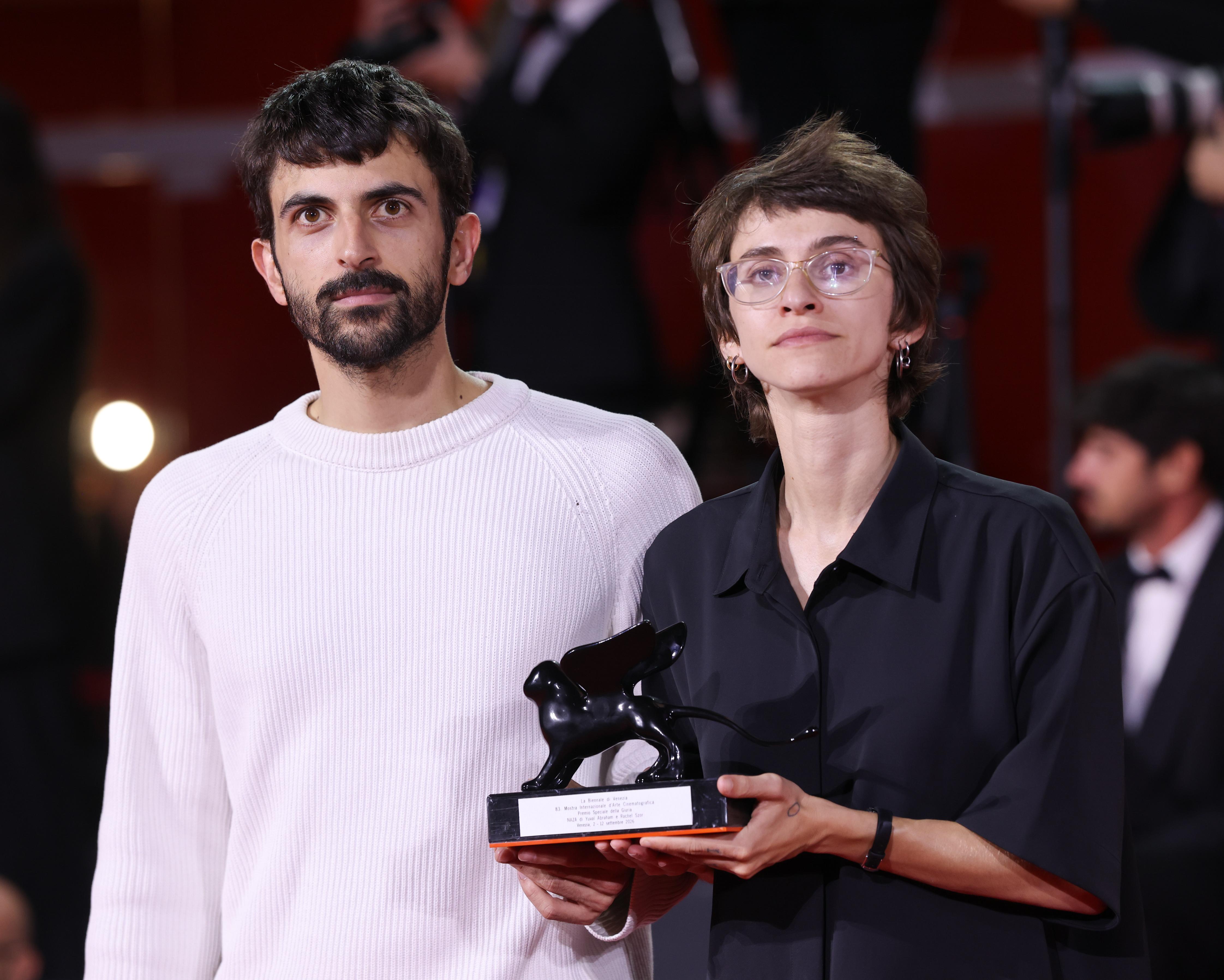 Two filmmakers stand together holding a black animal-shaped trophy at an awards ceremony.