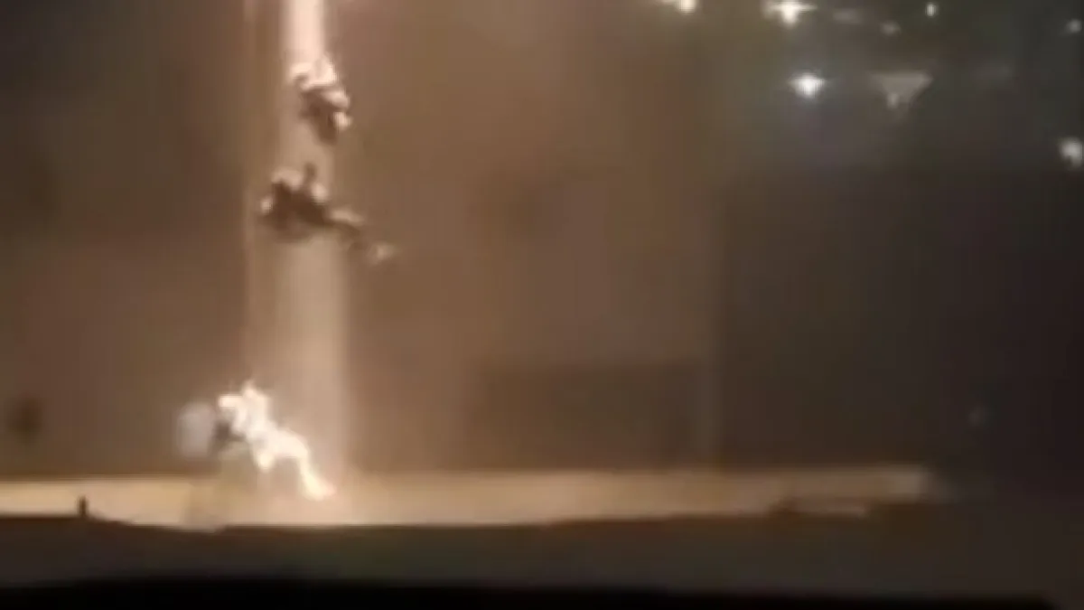 Blurry nighttime image shows figures rappelling from a helicopter near a brightly lit building.