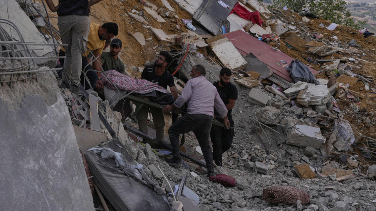Men carry a stretcher through rubble at a heavily damaged site.