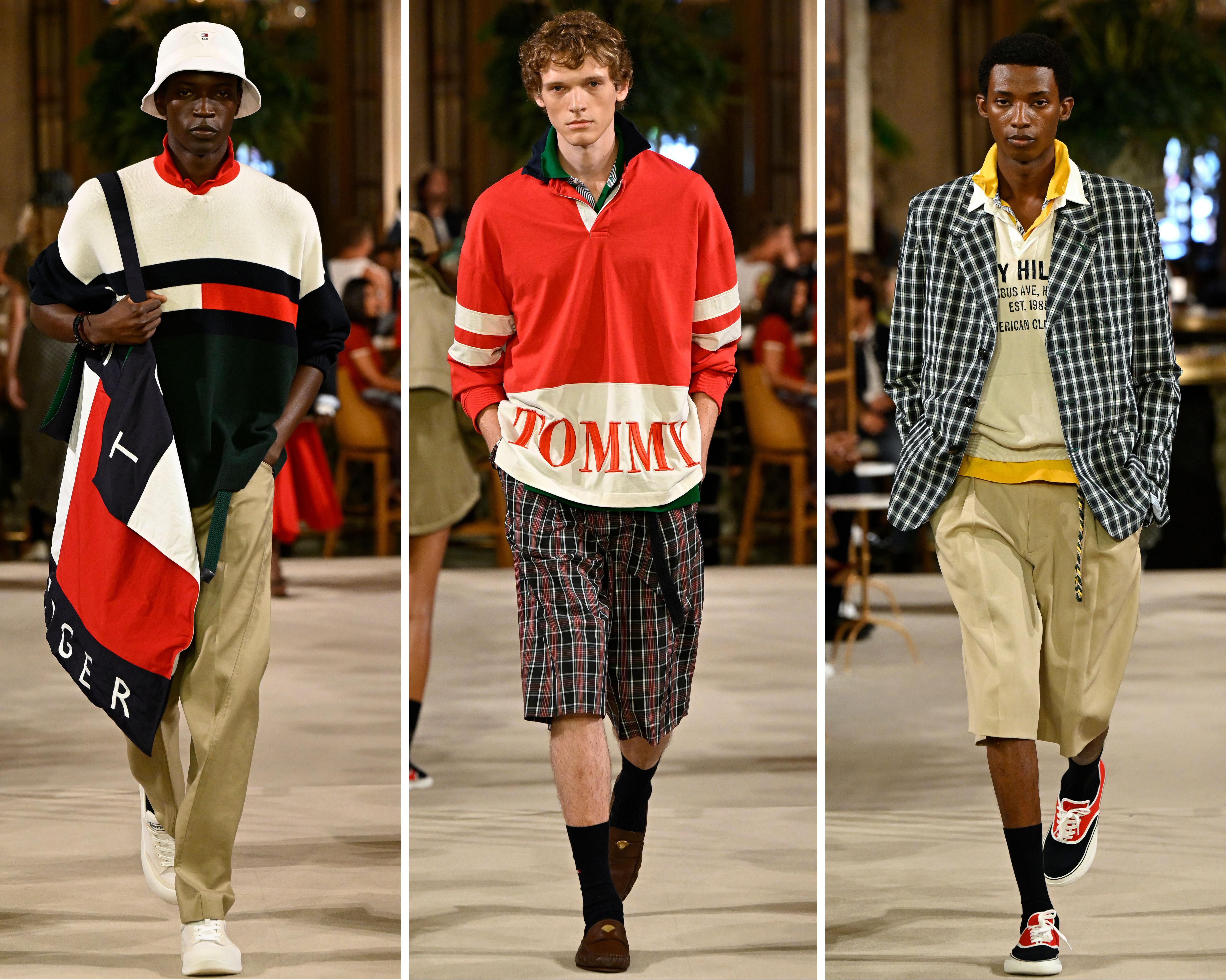 Three male models walk a runway wearing colorful Tommy Hilfiger-inspired outfits in a warmly lit interior.