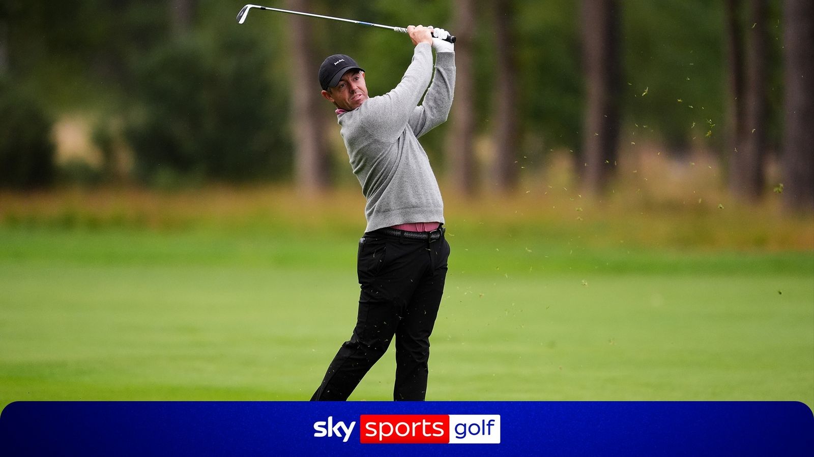 Golfer in grey sweater follows through on a shot as turf and leaves fly