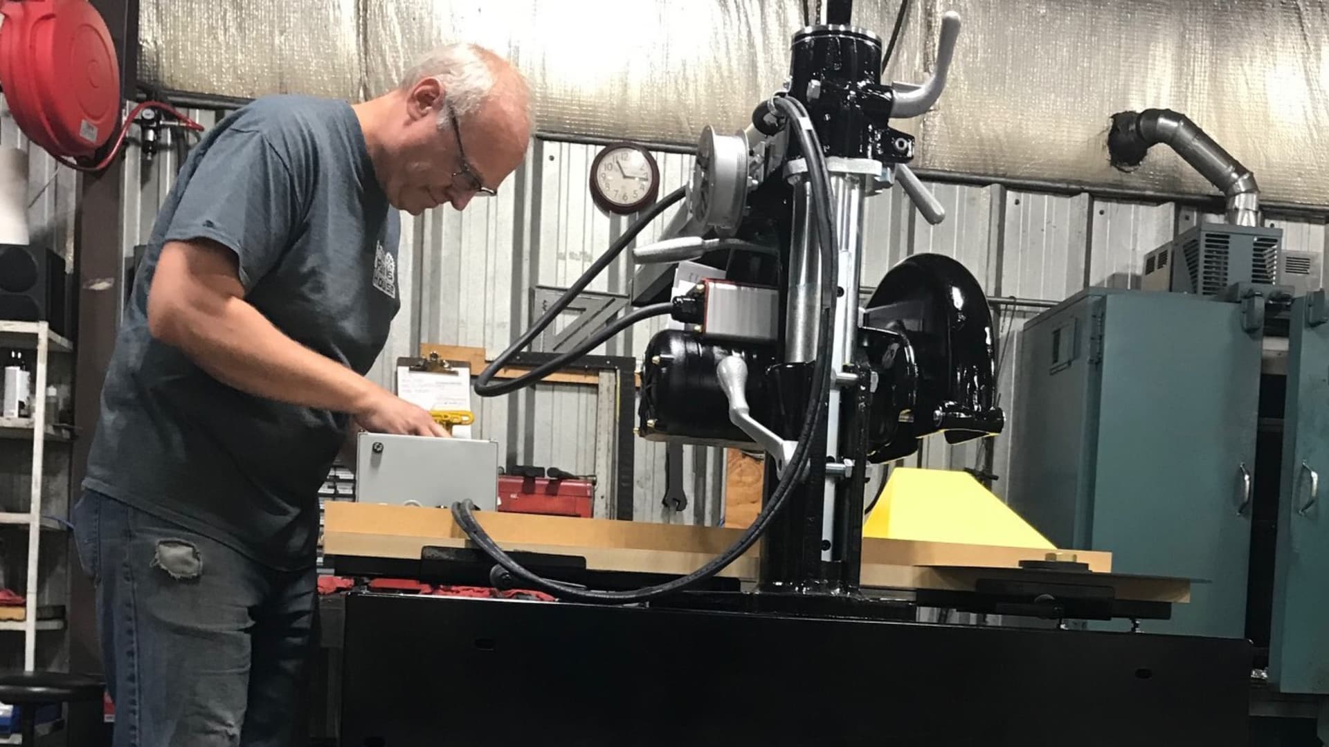 Man works on industrial machinery inside a workshop filled with tools, equipment and storage cabinets.