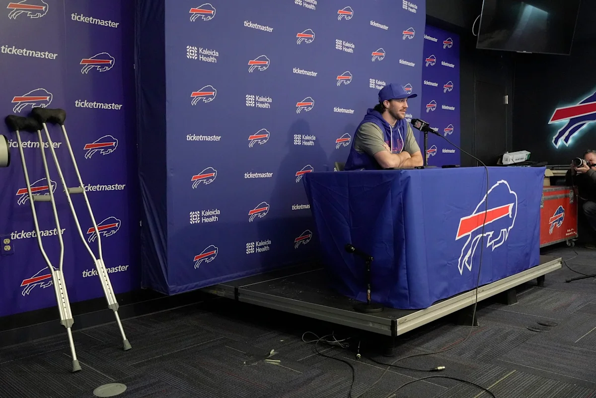 Football player seated at a press conference table beside crutches and microphones