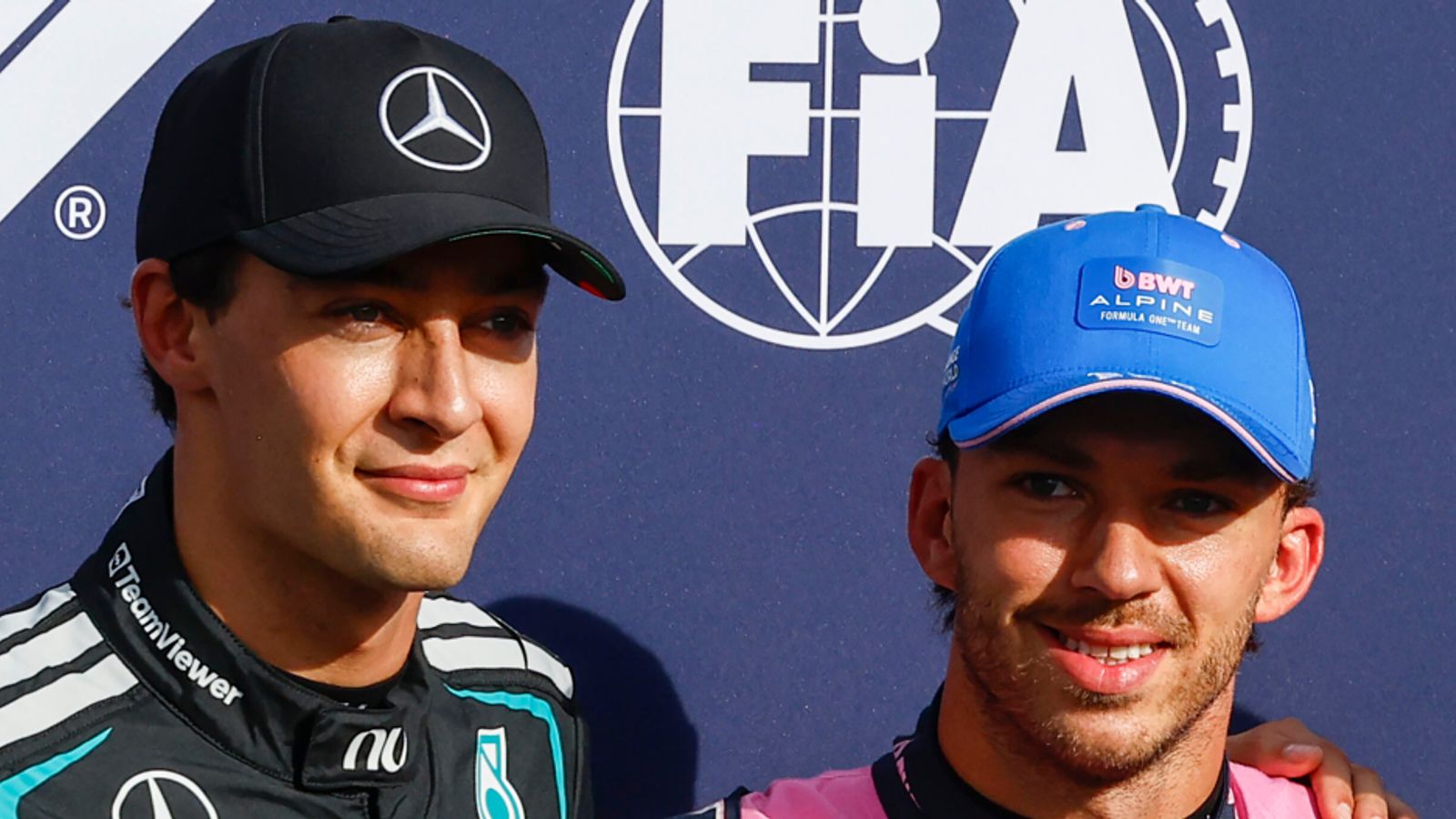 Two Formula One drivers in Mercedes and Alpine team gear pose together in front of an FIA backdrop.