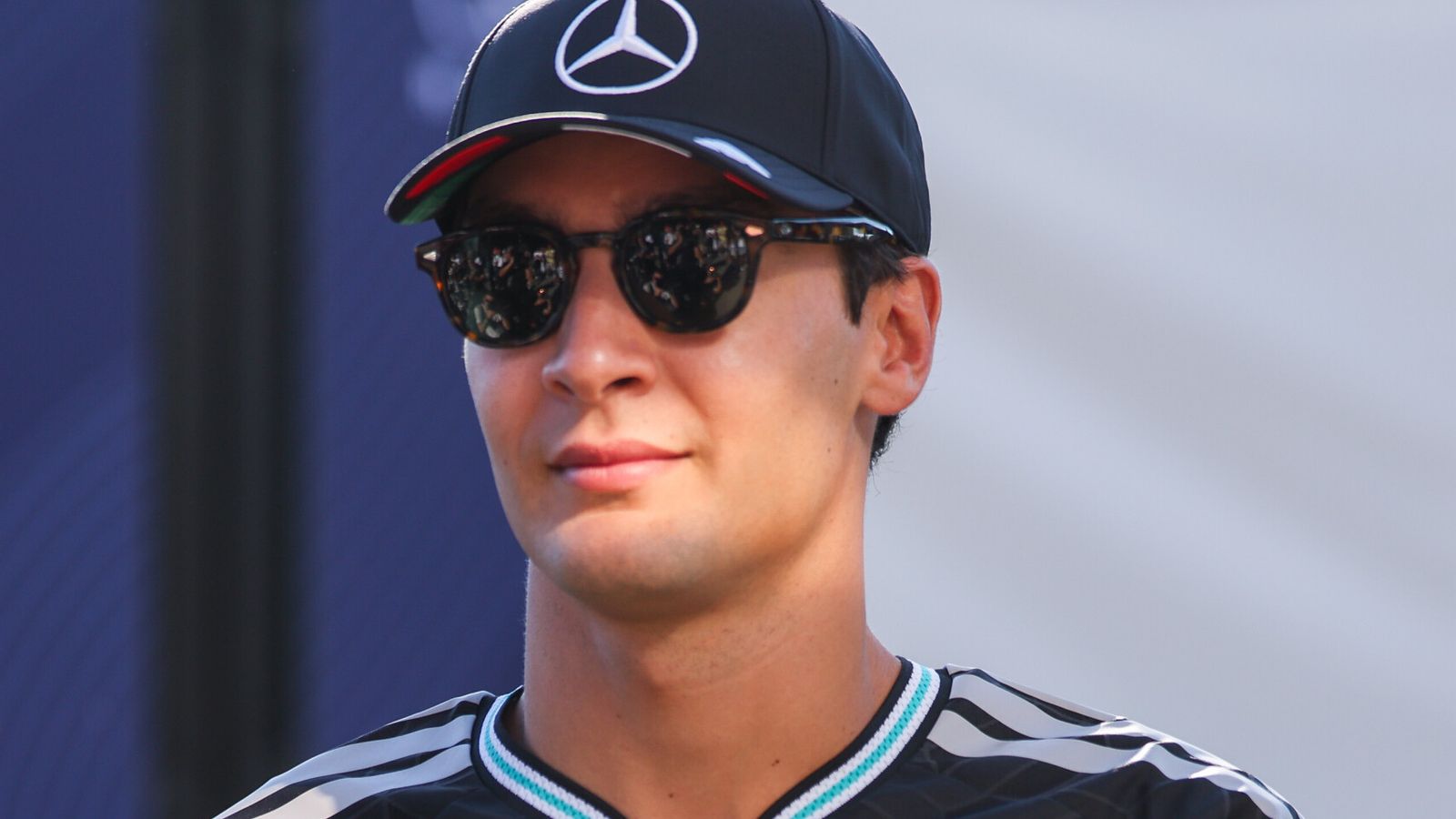 Close-up of a racing driver wearing a Mercedes cap, sunglasses and a black-and-white team shirt.