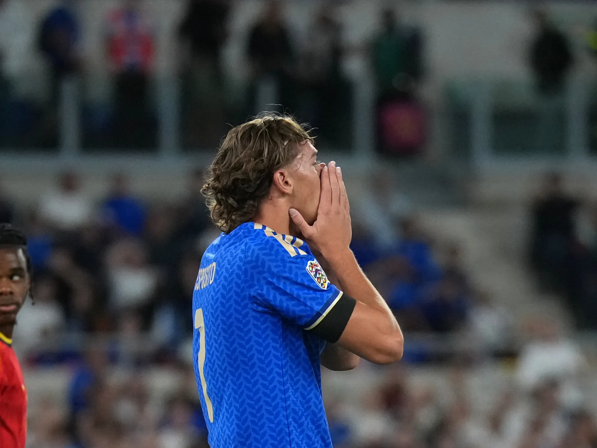 Italy player in blue covers his face with both hands during a match as an opponent watches nearby.