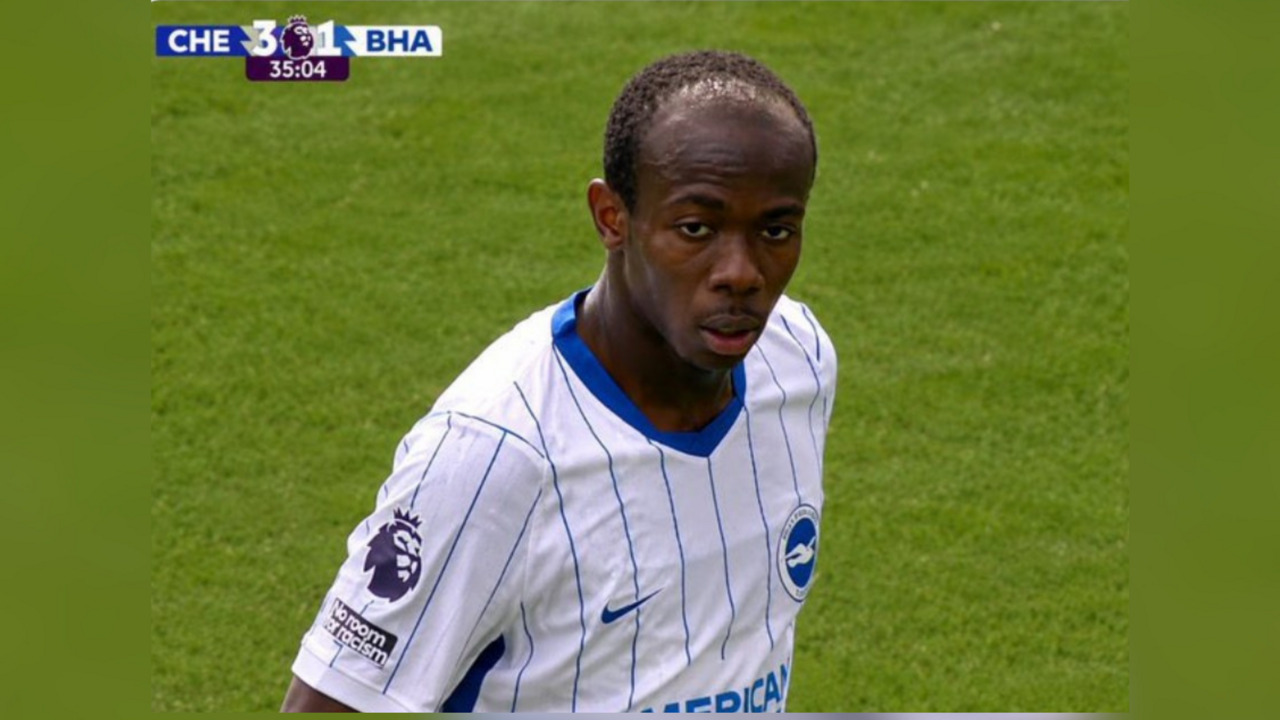 Footballer in white pinstriped Brighton jersey standing on a grass pitch during a match