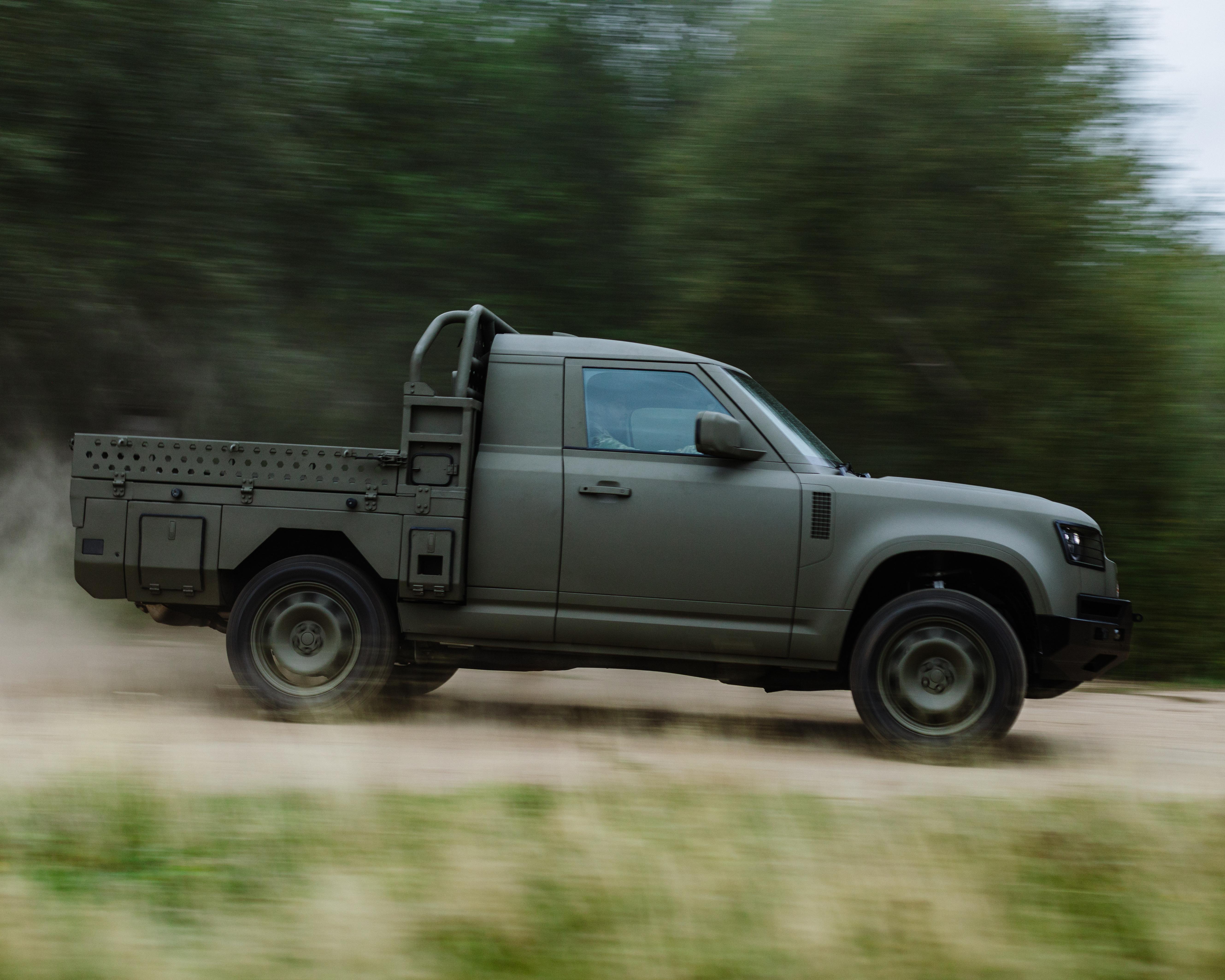 Gray utility pickup truck speeding along a dirt road with blurred trees behind it