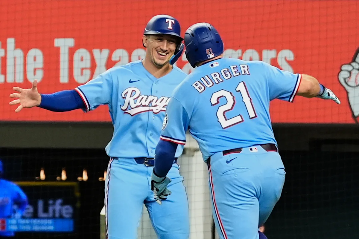 Two Texas Rangers players in blue uniforms celebrate near home plate during a game.