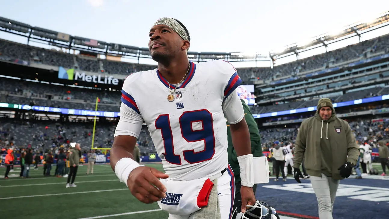 New York Giants quarterback in white uniform walking across a football field after a game