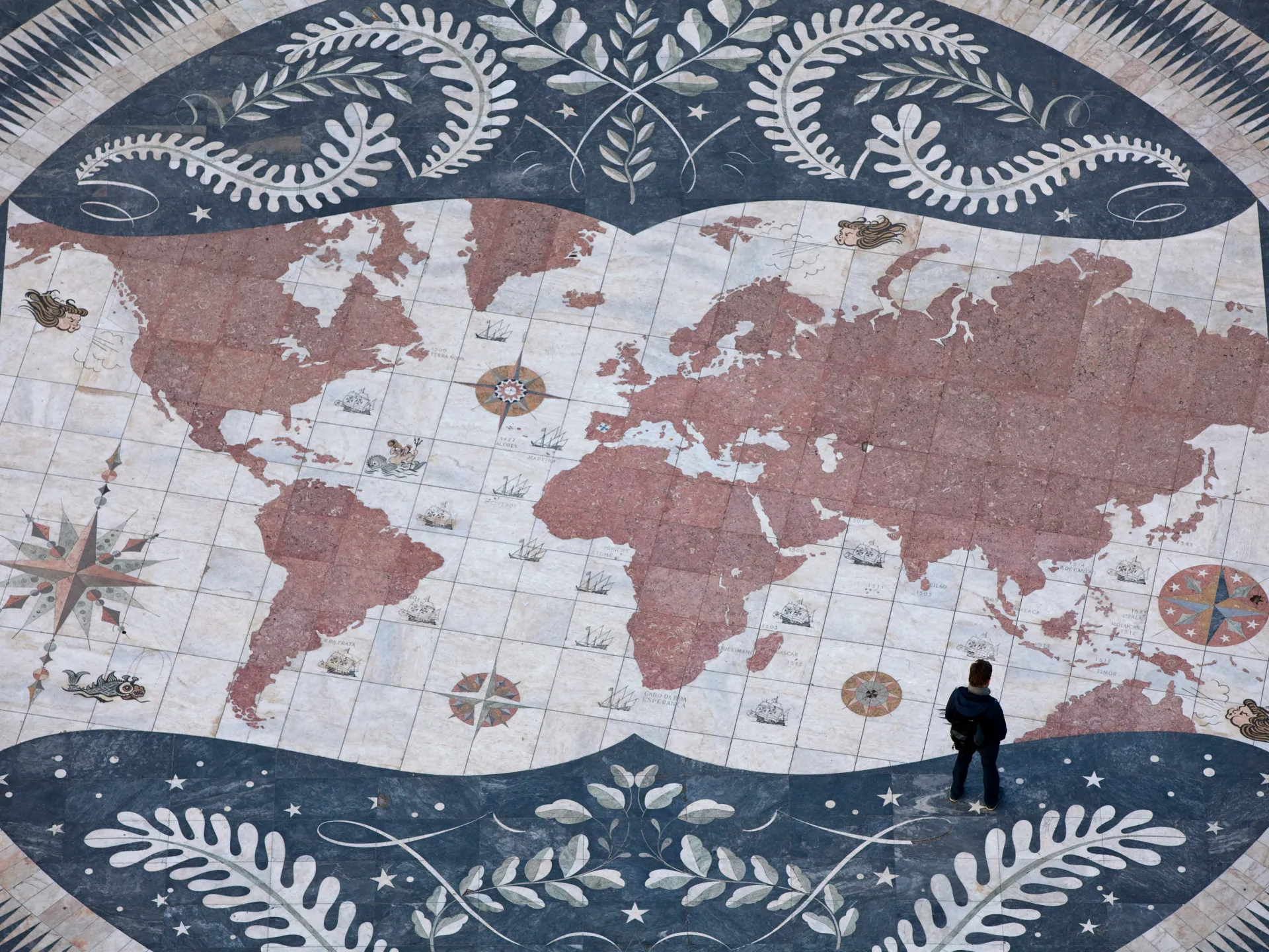Decorative floor map showing world continents, compass roses, ships and a person standing near Australia.