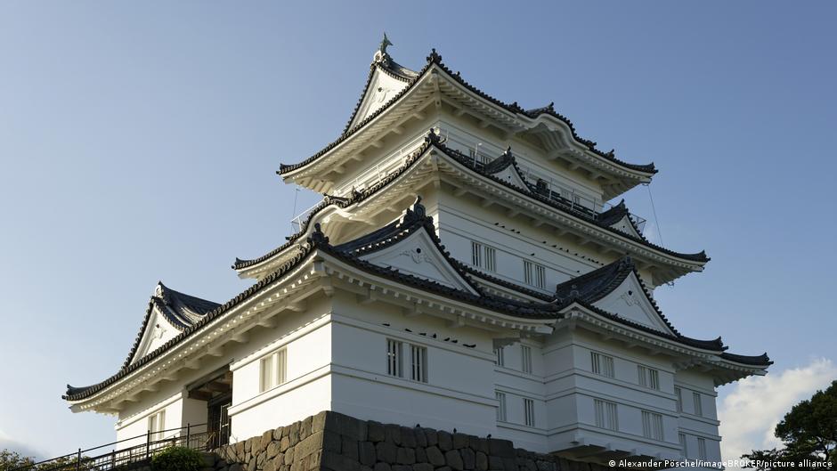 White traditional Japanese castle with ornate black roofs above a stone foundation under a clear blue sky