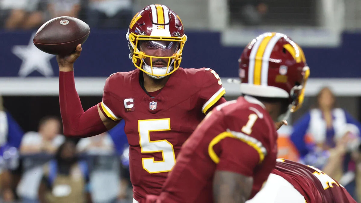 Washington quarterback in burgundy uniform holds football as teammate lines up during game