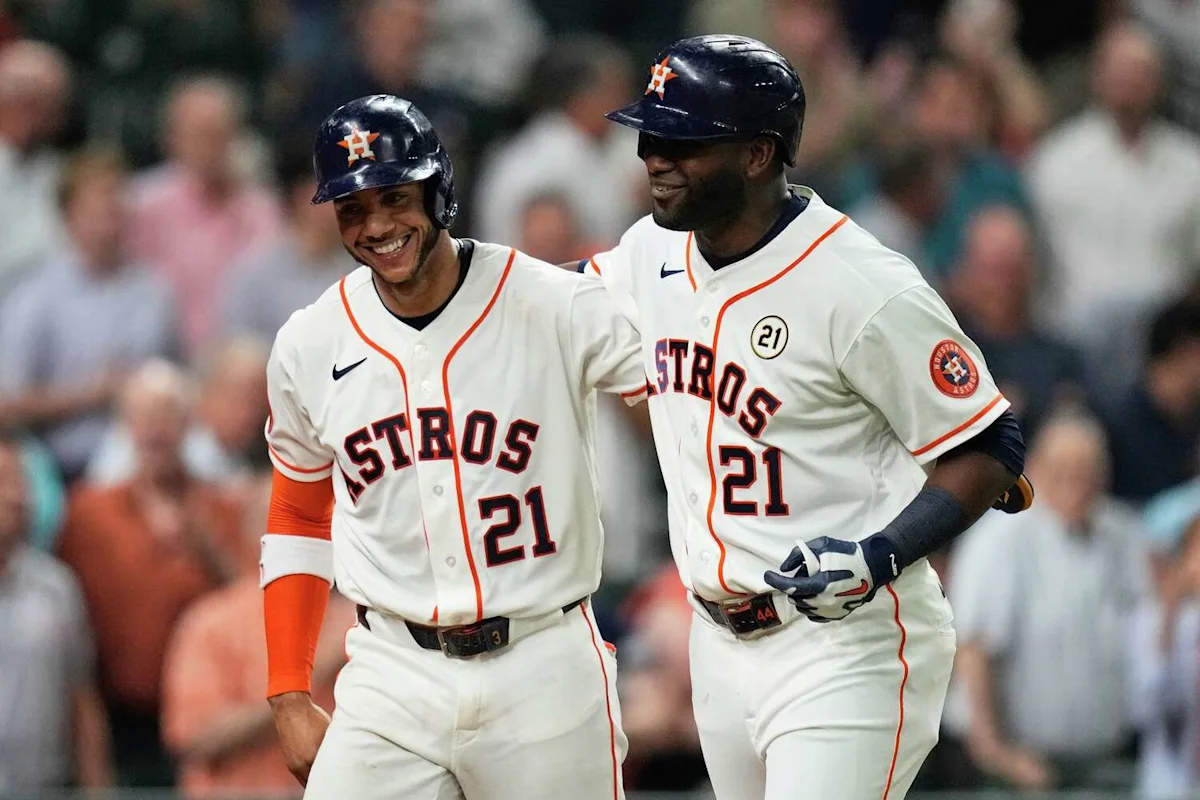Two Houston Astros players in white uniforms and helmets smile while walking together.