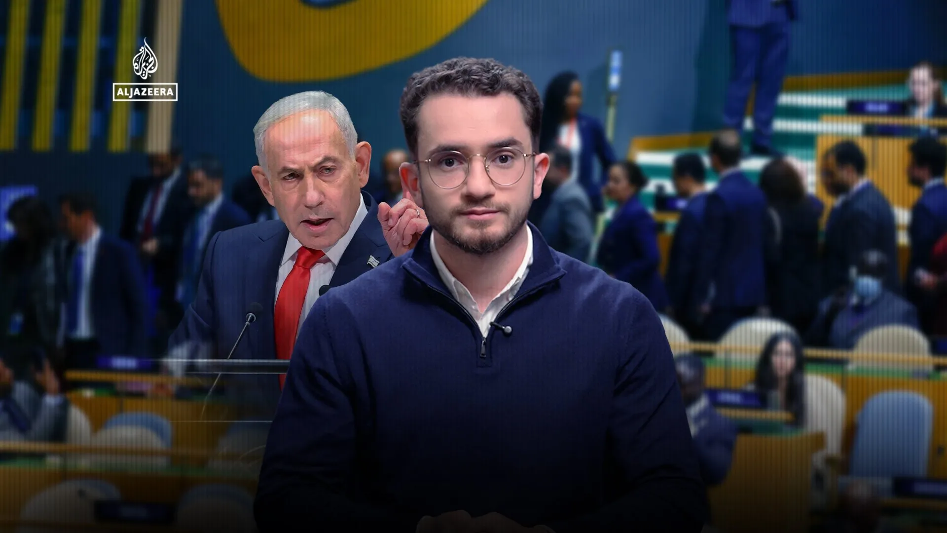 A bespectacled reporter stands before a blurred assembly hall, with an older man speaking at a lectern behind him.