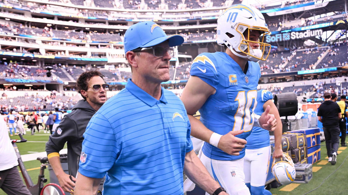 Chargers coach in a blue polo walks beside helmeted quarterback number 10 on the field.