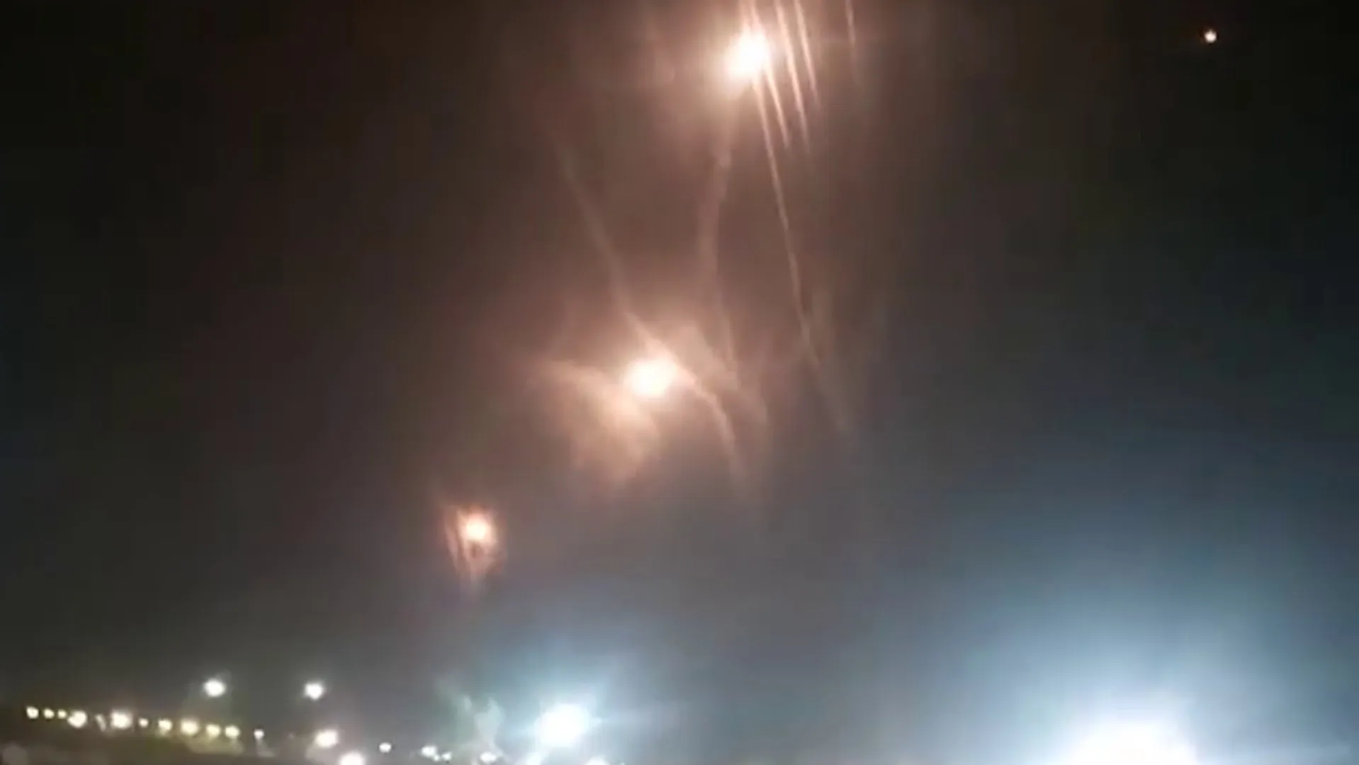 Blurry nighttime sky with several bright streaks and glowing points above distant lights