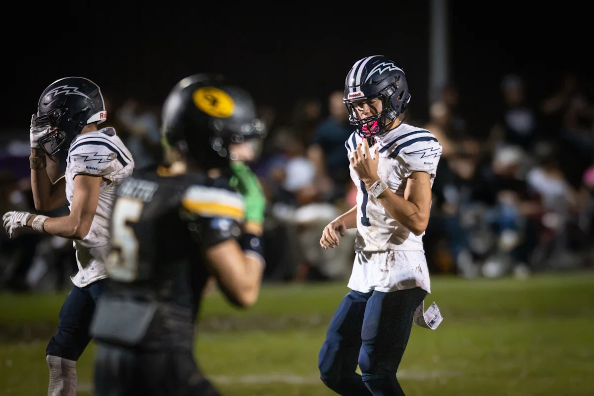 Two football players in white uniforms face an opposing player under stadium lights.