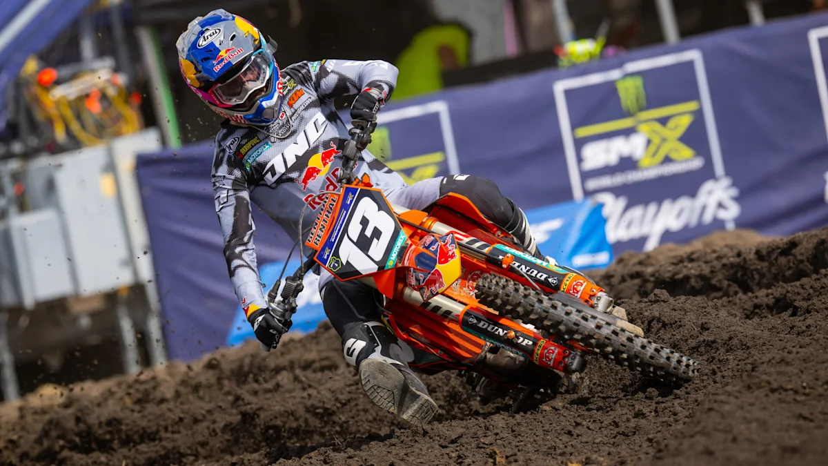 Motocross rider leans into a muddy turn on an orange KTM dirt bike numbered 3
