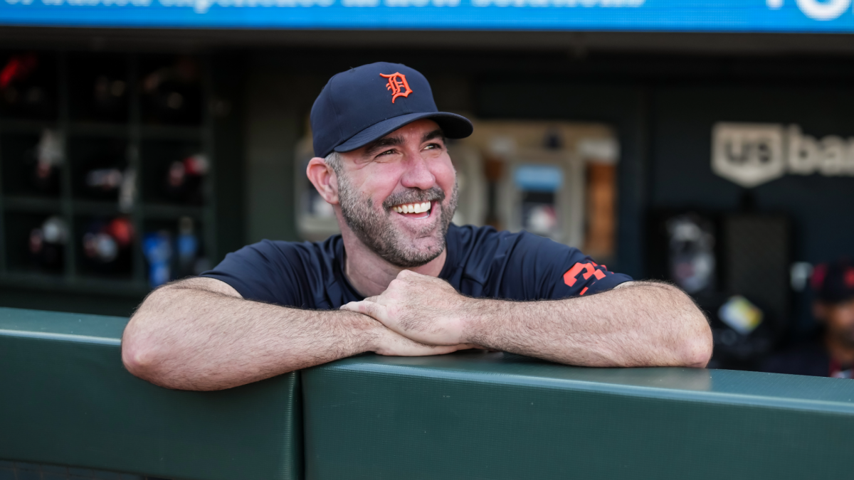 Smiling baseball player in a Detroit Tigers cap leans on the dugout railing.