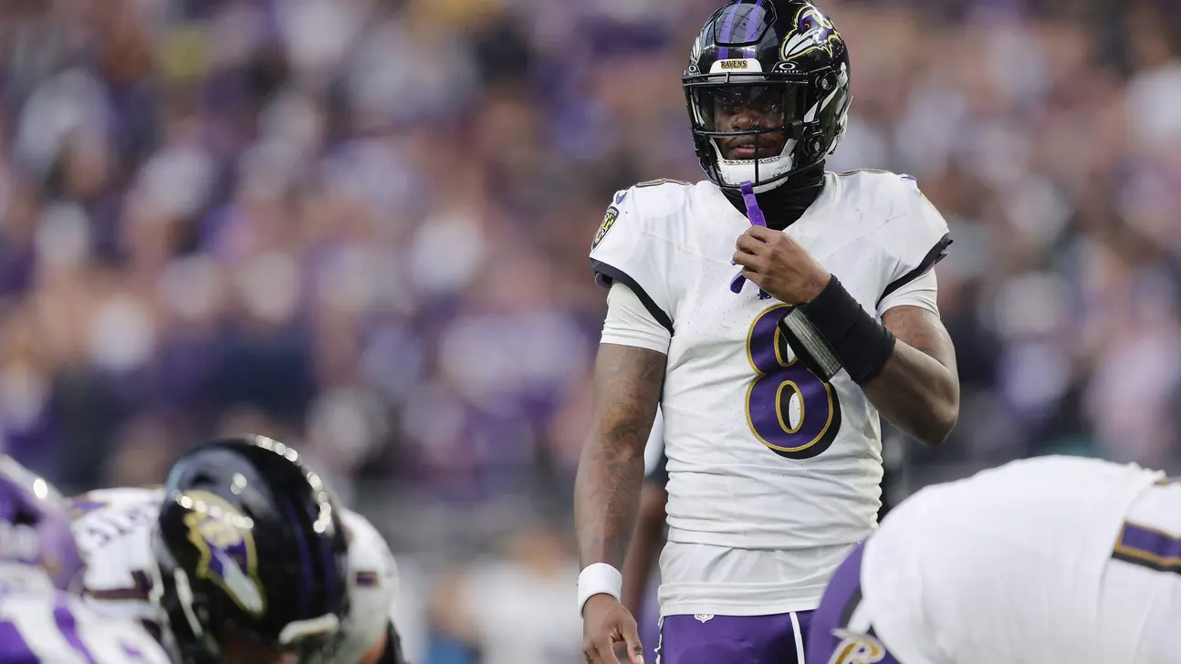 Football quarterback in Ravens uniform adjusts his chin strap during a game