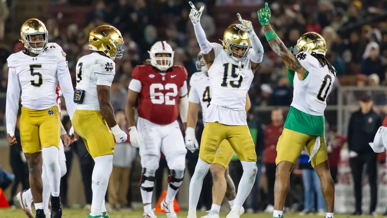 Notre Dame football players in white and gold celebrate during a game against opponents in red uniforms.