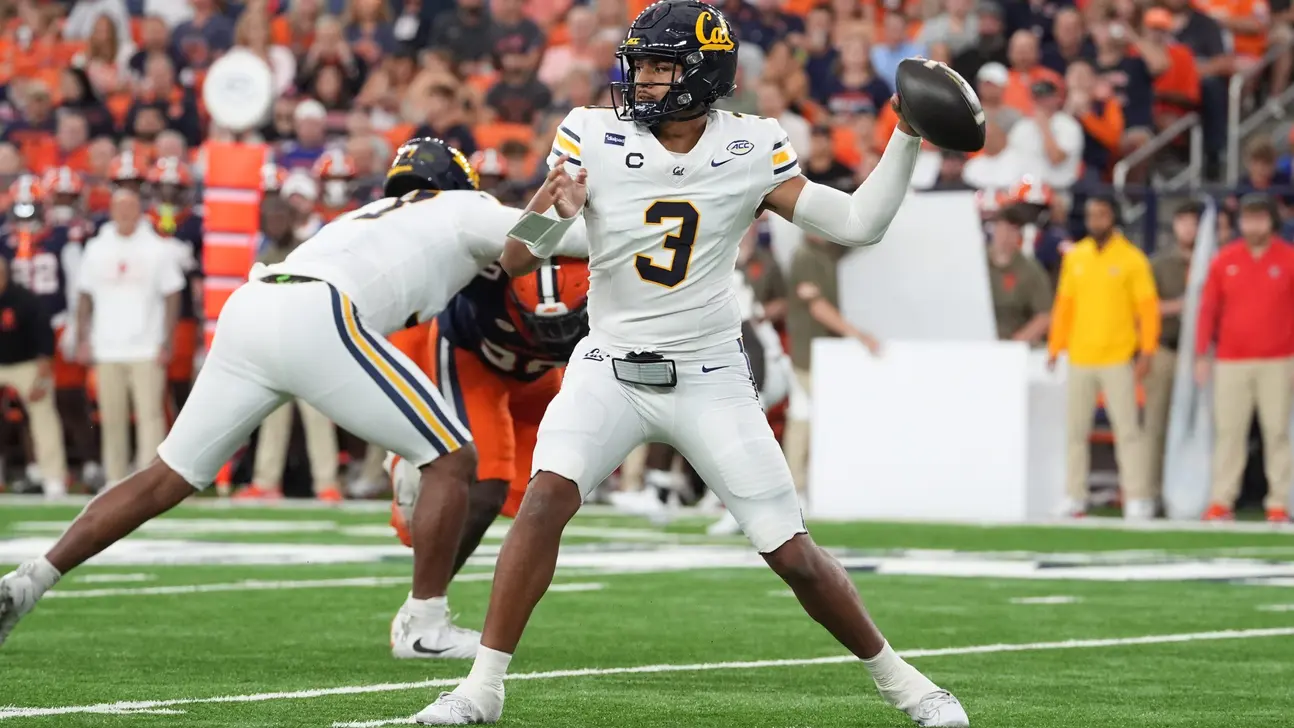 California quarterback in a white number 3 uniform prepares to throw as a teammate blocks a Clemson defender.