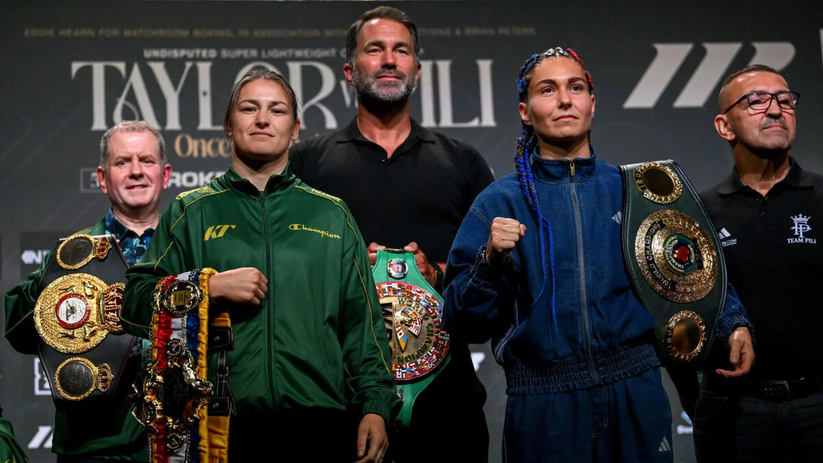 Two female boxers pose with championship belts alongside three men at a fight event.