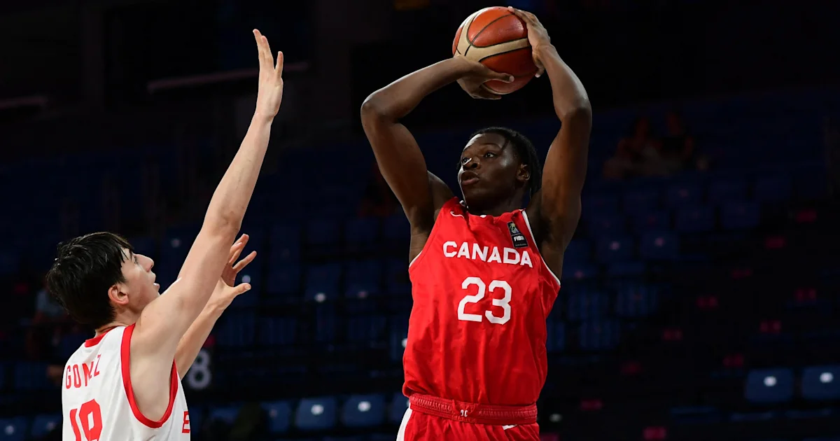 A Canadian player raises a basketball over his head as a defender reaches up beside him.