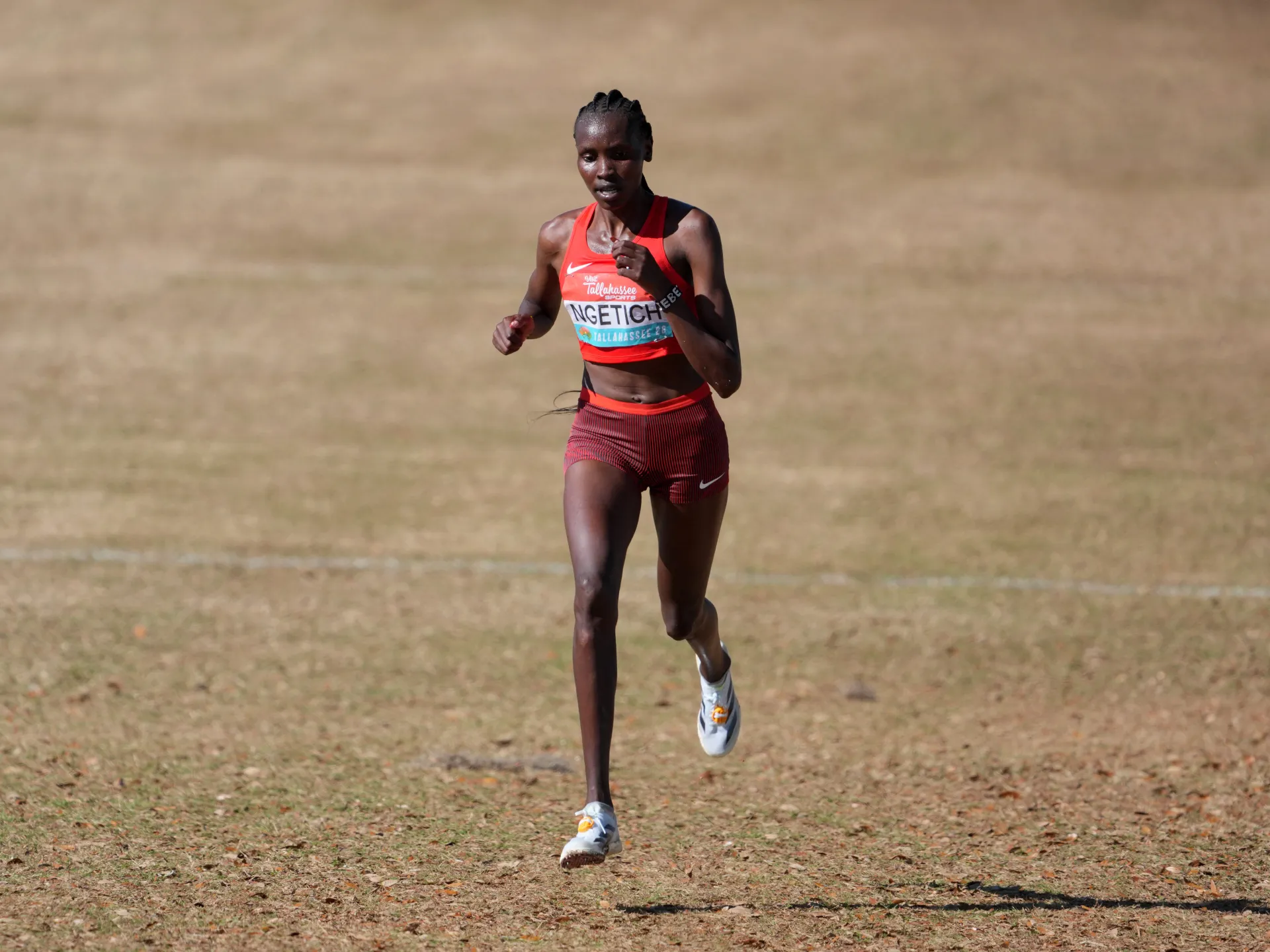 Female runner in red racing kit running across a dry grassy field