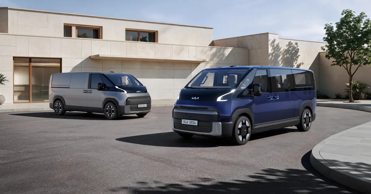 Two Kia electric vans parked outside a modern white residential building under clear daylight