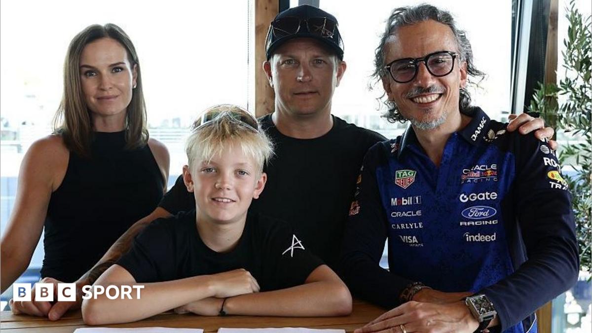 Four people pose indoors, including a young boy and a man wearing a Red Bull racing shirt.