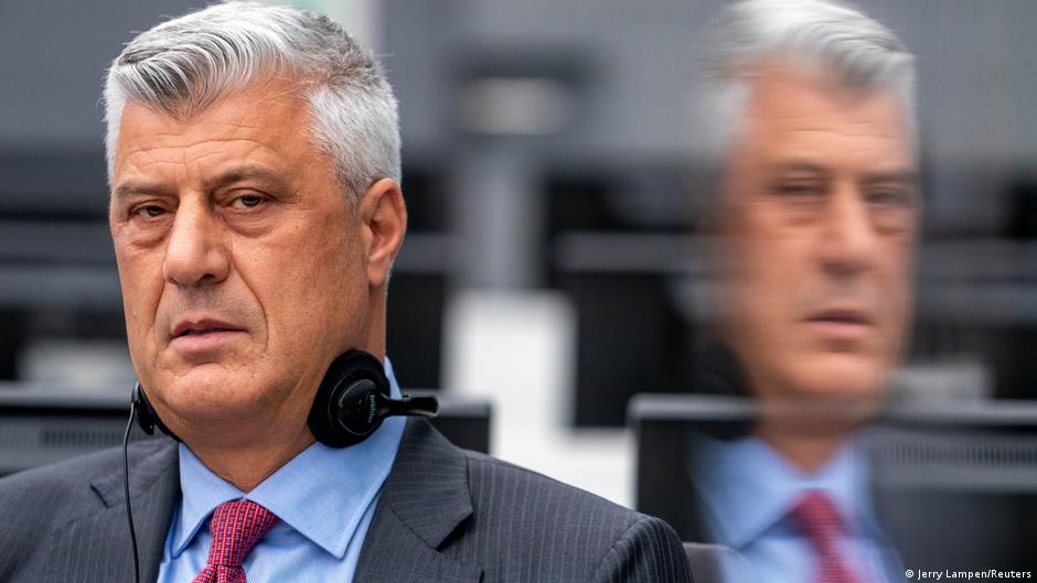 Gray-haired man in a suit wearing headphones, with a blurred duplicate figure behind him