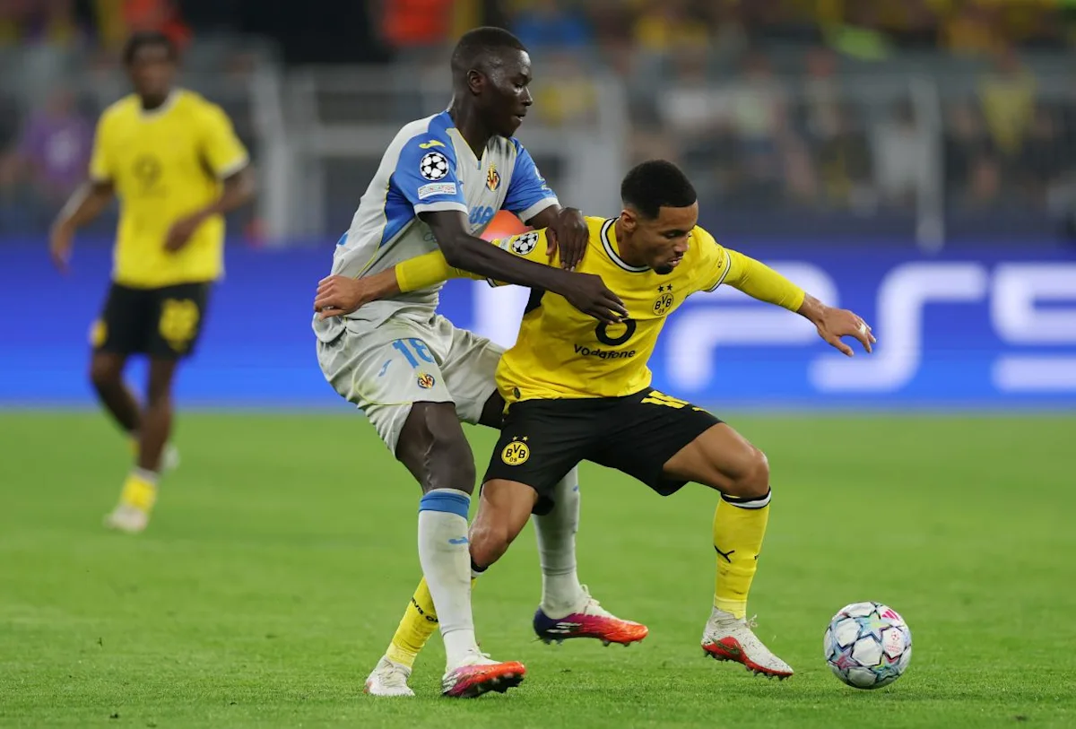 Footballers in yellow and white kits compete for the ball during a match.